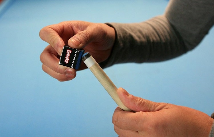 player puts chalk on tip of pool cue